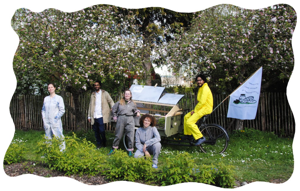 Image description: the team members of The Outsiders are posing in front of the Travelling Farm Museum bicycle underneath an apple tree. 