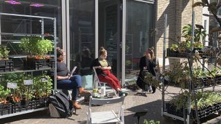 Image Description: Three people are sitting on chairs outside the depot in the Terwijde Winkelcentrum, they are surrounded by plants and pots that come from the plant farm Stekkers, and that can be bought directly from the depot.
